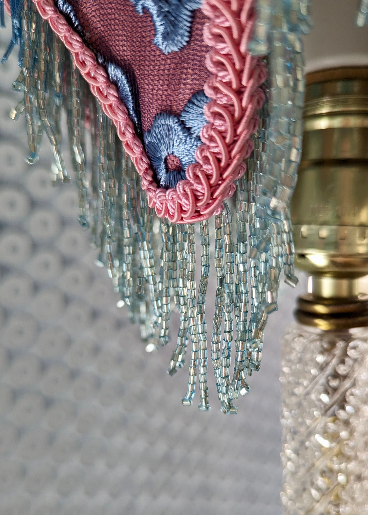 A close-up photo of a pink and blue lamp with an iridescent blue glass bead fringe. 